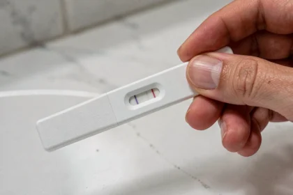 Main de femme tenant un test de grossesse avec une barre d'évaporation ambiguë sur un comptoir de salle de bain blanc