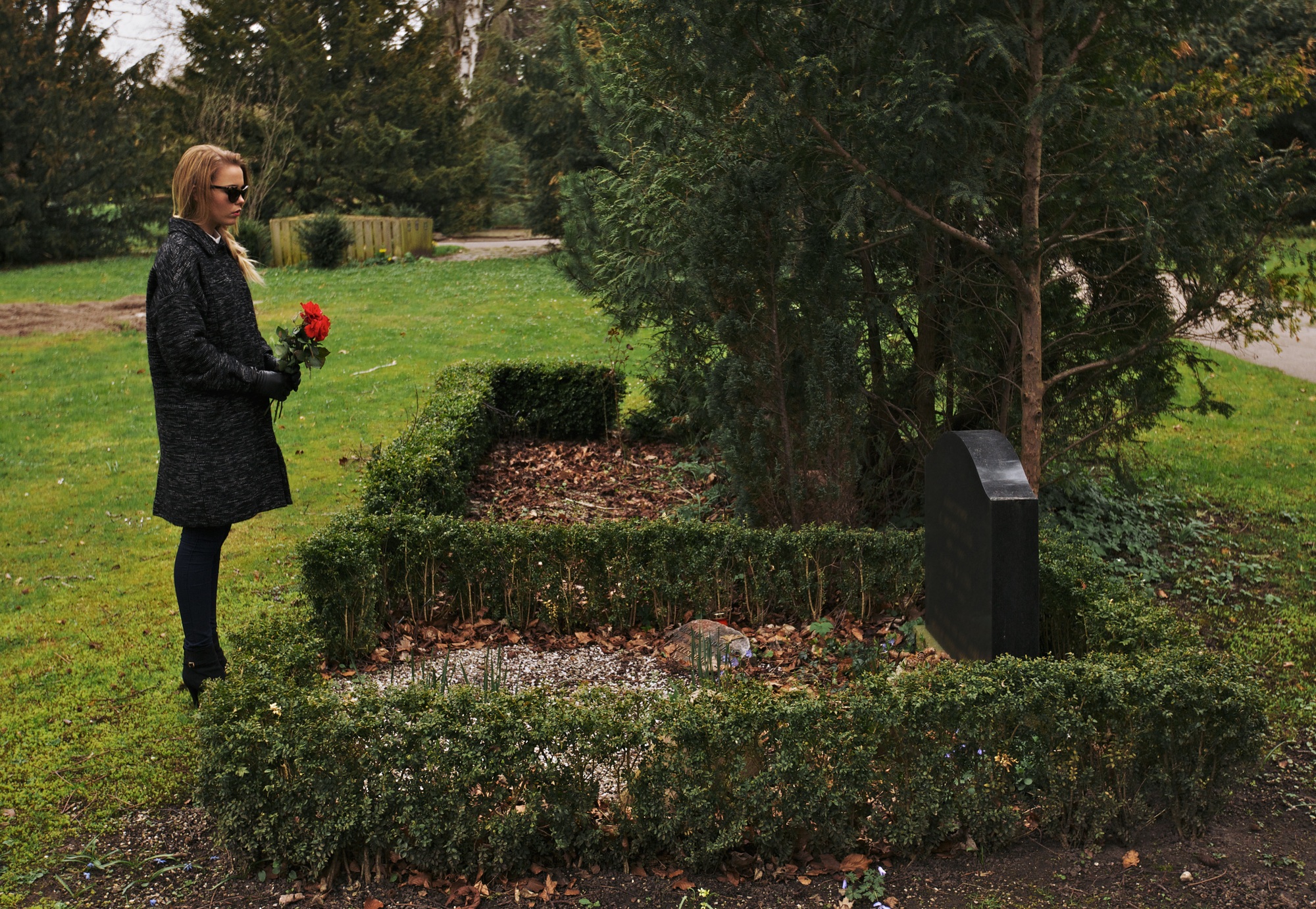 Young woman grieving at cemetery holding flowers